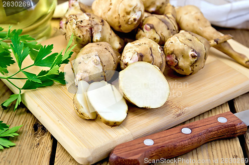 Image of Jerusalem artichoke is sliced with a knife on board