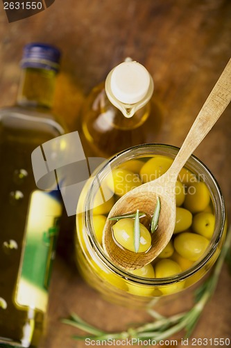 Image of Close up green olives in bank,  bottle of olive oil, rosemary