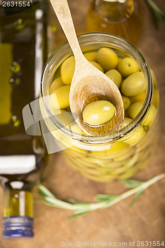 Image of Close up green olives in bank,  bottle of olive oil, rosemary