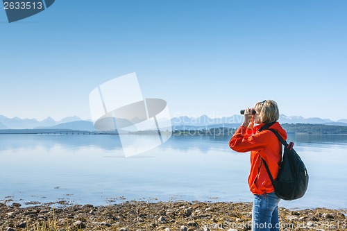 Image of Woman tourist looking through binoculars at distant Atlantic Road, Norway