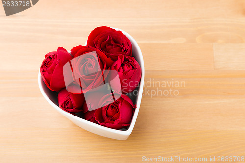 Image of Red rose inside the heart shape bowl on wooden background