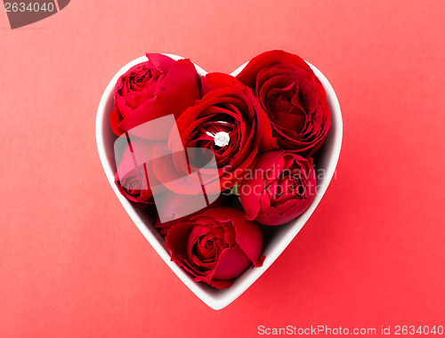 Image of Rose and diamond ring inside heart shape bowl over the red backg