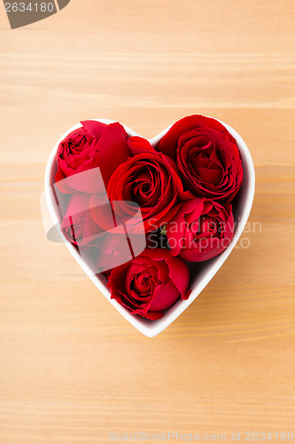 Image of Red rose inside heart shape bowl on wooden background