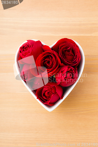 Image of Red rose inside heart shape bowl on wooden background