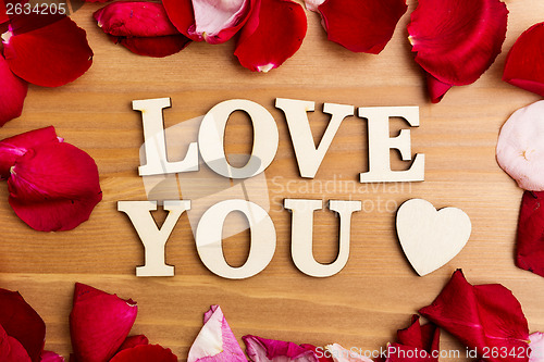 Image of Wooden letters forming phrase Love You with rose petal besides