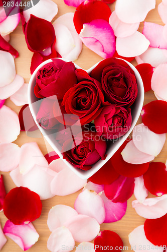 Image of Beautiful Red rose inside the heart shape bowl with petal beside