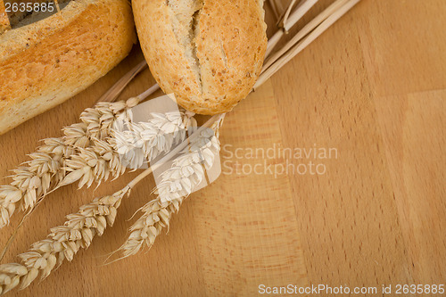 Image of roll on wooden table with ears of wheat grain