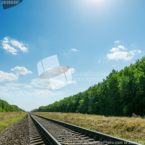 Image of railroad to horizon in green landscape and blue sky with sun ove