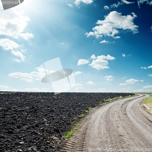 Image of sun in dramatic sky over road near black field