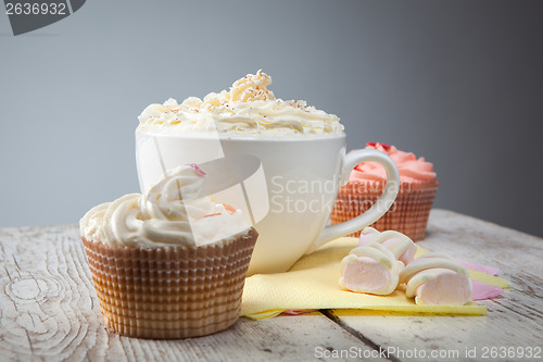 Image of hot chocolate with marshmallows, cream and cupcakes on wooden ba