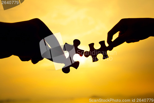 Image of Silhouette of two hands connect puzzle together 