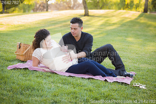 Image of Pregnant Hispanic Couple with Piggy Bank on Belly in Park