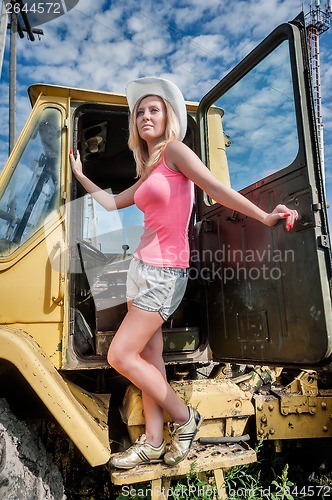 Image of Young attractive woman on old big tractor