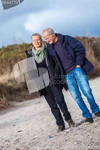 Image of mature senior couple walking on the beach autumn winter