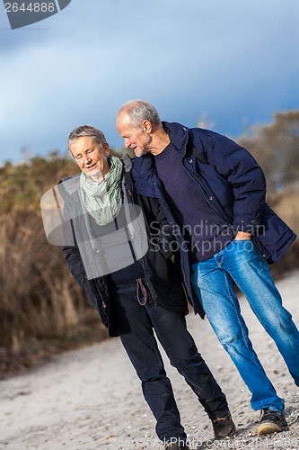 Image of mature senior couple walking on the beach autumn winter