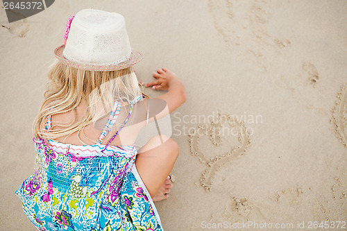 Image of Young girl drawing heart shapes in sand