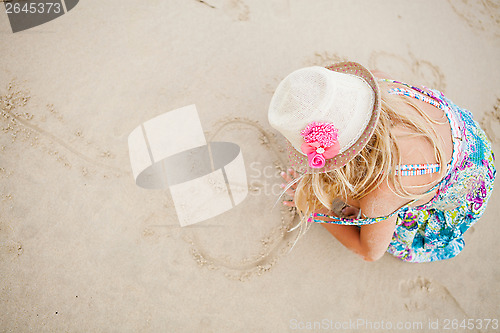 Image of Young girl drawing heart shapes in sand