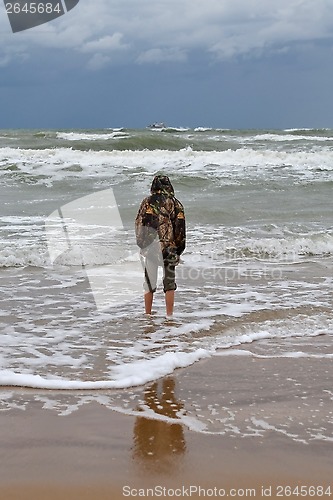 Image of The teenager costs on the seashore in rainy weather a back in a 