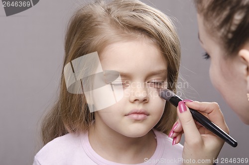 Image of Makeup artist deals powder on face of girl