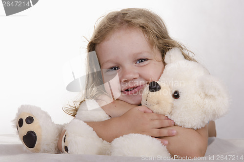 Image of Two-year-old girl lies and bear hugs