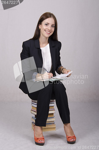 Image of School teacher sitting on books checks notebooks students