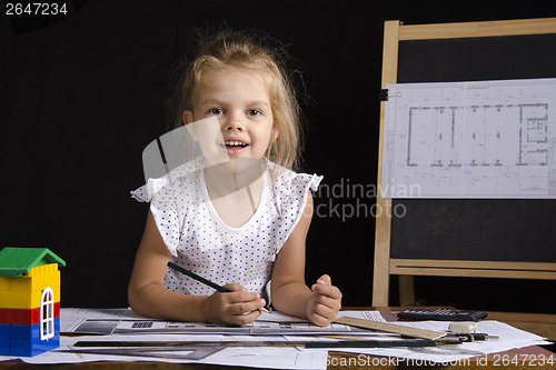 Image of Girl-architect sitting behind Desk and looks in frame