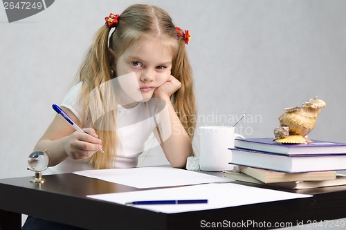 Image of girl writes on a piece of paper sitting at table in image writer