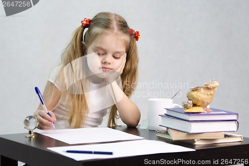 Image of girl writes on a piece of paper sitting at table in image writer