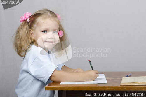 Image of Little girl sitting at table and wrote in notebook