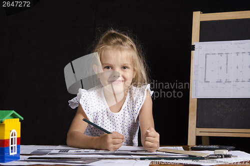 Image of Girl-architect sitting behind Desk and looks in frame
