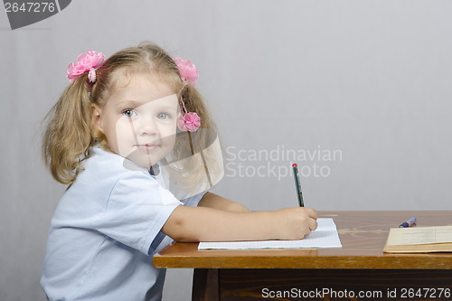 Image of Little girl sitting at table and wrote in notebook