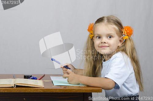 Image of Little girl sitting at table and wrote in notebook