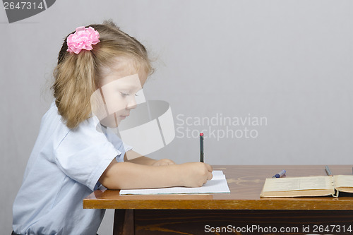 Image of Little girl sitting at table and wrote in notebook