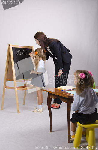 Image of At blackboard girl with tutor draw shapes, another sitting table