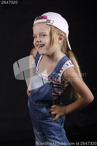 Image of Portrait laughing four-year girl in overalls and cap