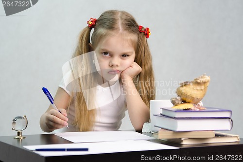 Image of girl writes on a piece of paper sitting at table in image writer