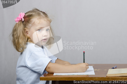 Image of Little girl sitting at table and wrote in notebook