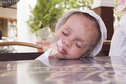 Image of Two-year-old girl asleep at a table in street cafe