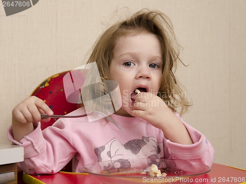 Image of Two-year-old girl eats with a fork at table in kitchen