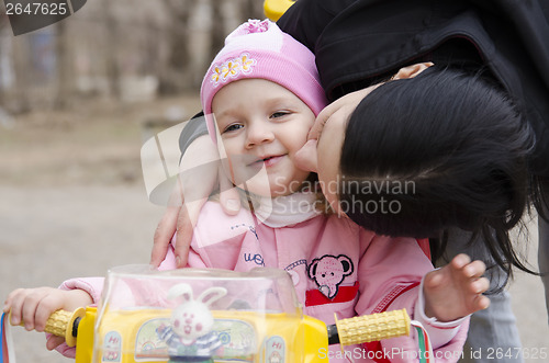 Image of little girl sitting on a bike kissed my mother