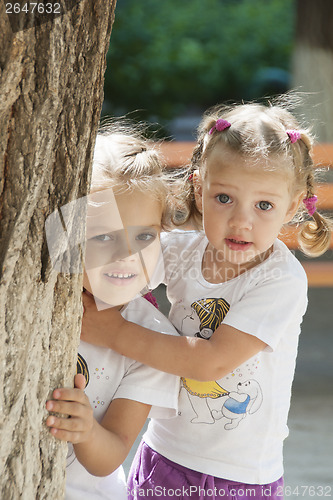 Image of Two children peep out from behind a tree