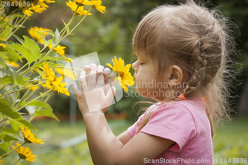 Image of Three-year girl sniffing yellow flower