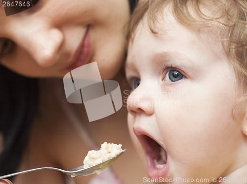 Image of mother is feeding small child porridge with spoon