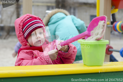 Image of little girl pours sand bucket in sandbox