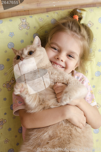 Image of little girl hugging cat lying on a mattress floor