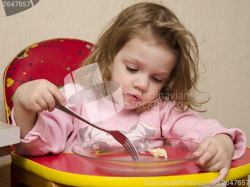Image of Two-year-old girl eats with a fork at table in kitchen