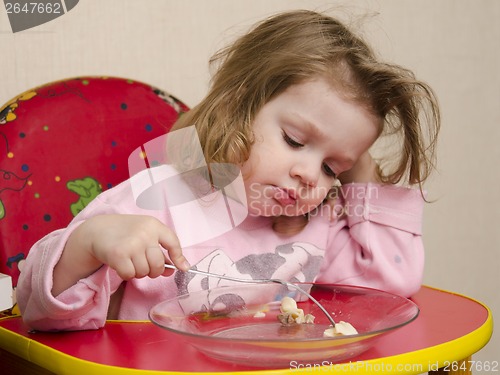 Image of Two-year-old girl eats with a fork at table in kitchen