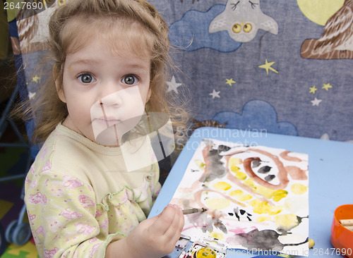 Image of Two-year-old girl is painting at table and looks