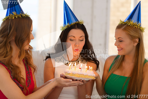 Image of three women wearing hats holding cake with candles