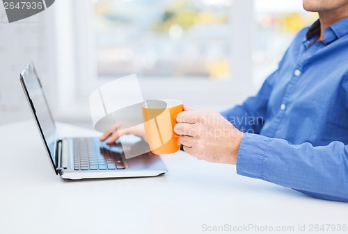 Image of male hand with cup of tea or coffee and laptop